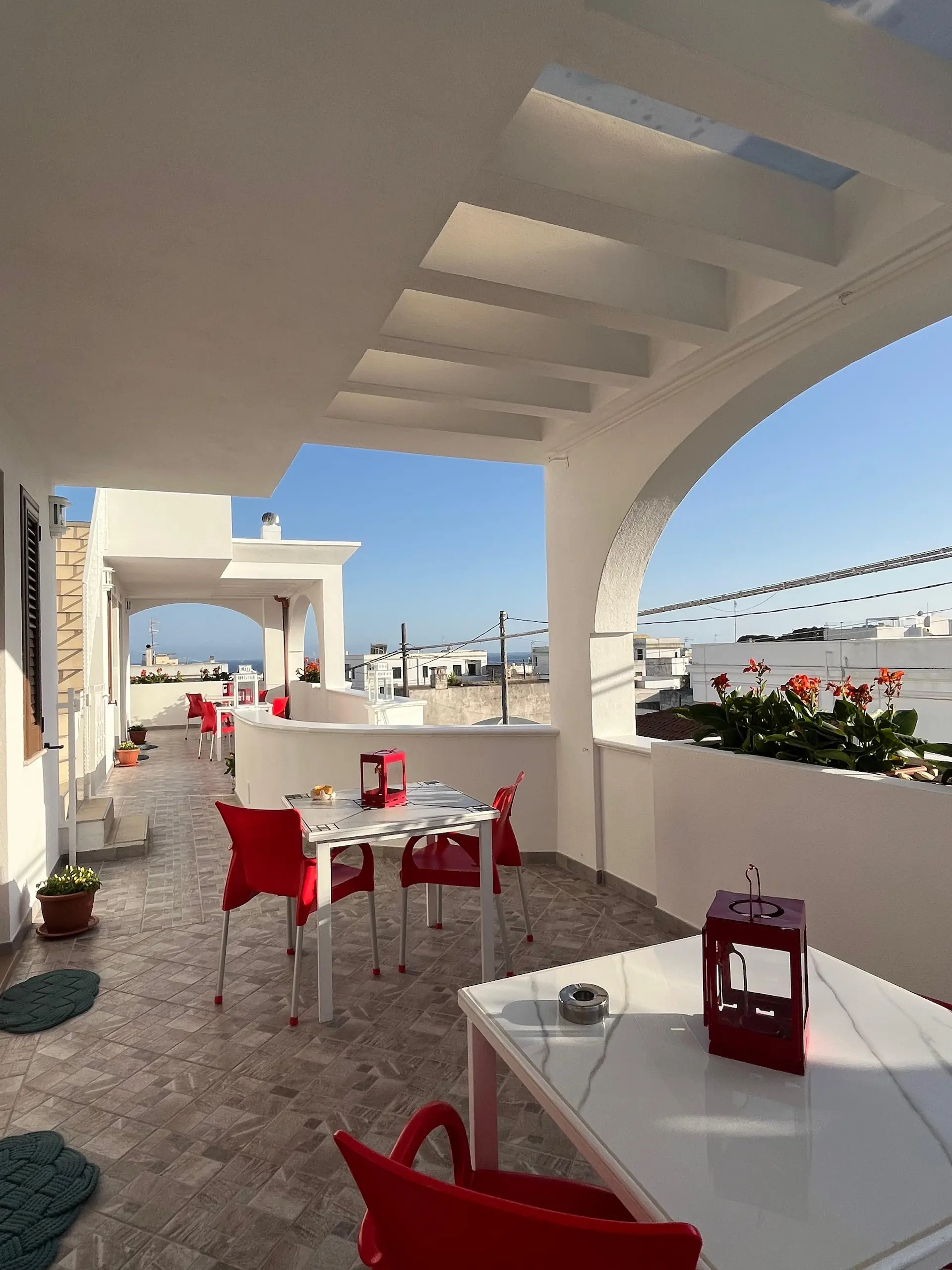 Veranda panoramica con fiori, tavoli bianchi e sedie rosse con vista sul mare - atmosfera rilassante a Santa Maria di Leuca